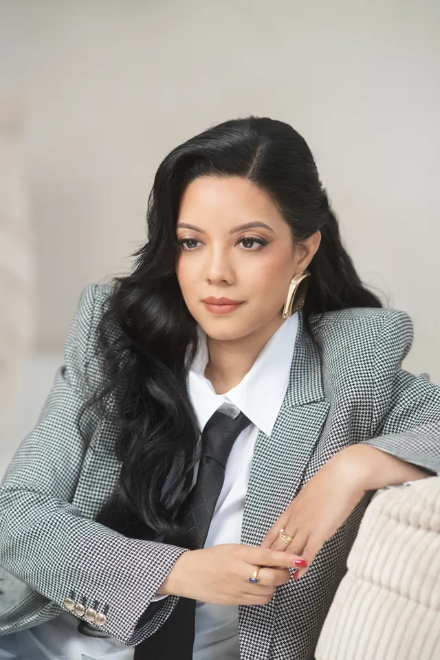Priscilla Laclé in a checked blazer, leaning on a sofa
