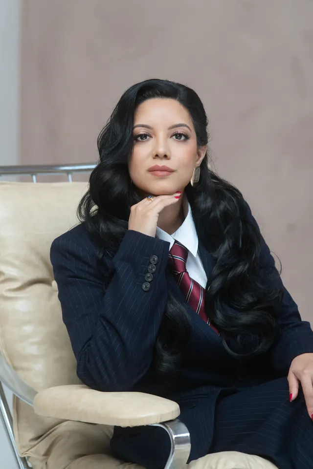 Priscilla Laclé in a navy suit, seated, with her hand at her chin