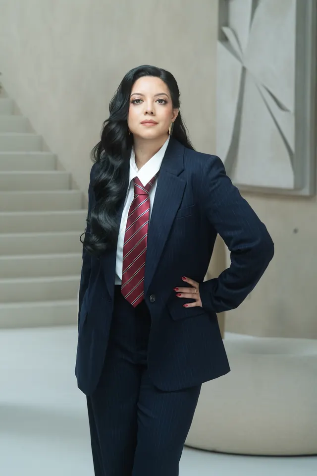 Priscilla Laclé standing in a navy pinstripe suit with a red striped tie